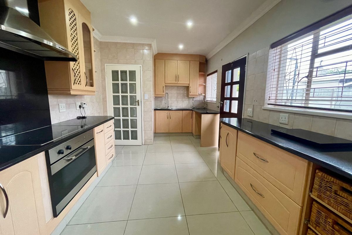 A well-maintained kitchen featuring light wood cabinetry, dark granite countertops, integrated stainless steel appliances, and neutral ceramic floor tiling.