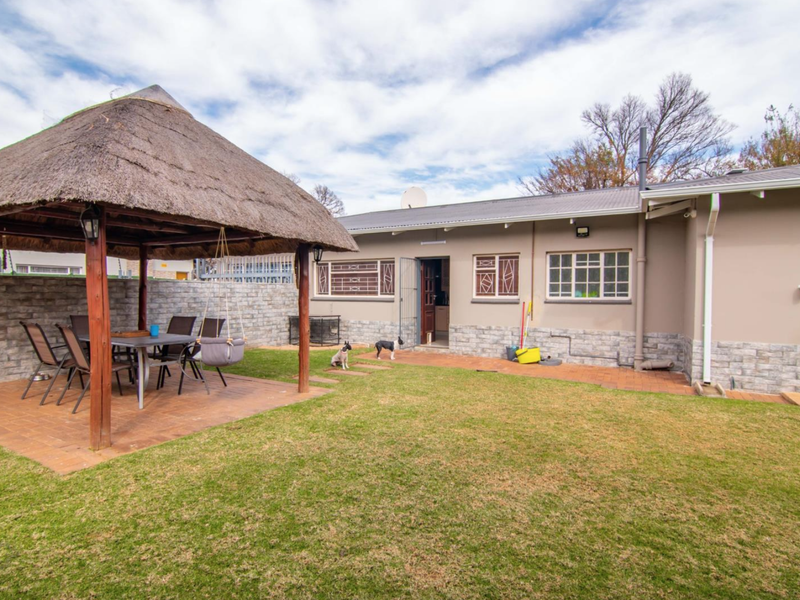 Rear garden view featuring a thatched gazebo, brick-paved patio area, and stone-clad exterior walls with security-fitted windows.