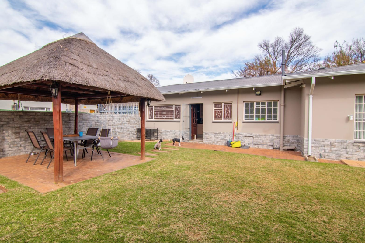 Rear garden view featuring a thatched gazebo, brick-paved patio area, and stone-clad exterior walls with security-fitted windows.