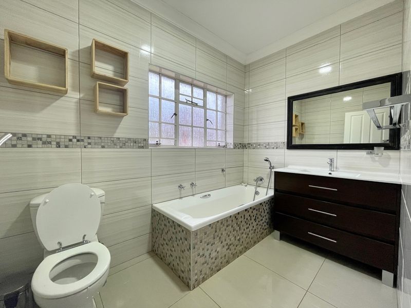 A well-maintained bathroom featuring modern tiled walls, a built-in vanity, a bathtub, and a toilet.