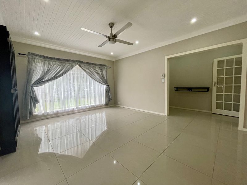 A bright, spacious living area featuring polished tiled floors, a ceiling fan, and a classic tongue and groove ceiling with recessed lighting.