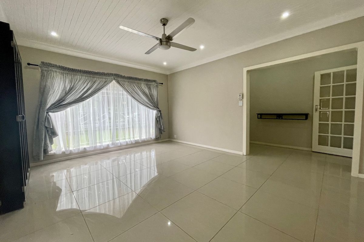 A bright, spacious living area featuring polished tiled floors, a ceiling fan, and a classic tongue and groove ceiling with recessed lighting.