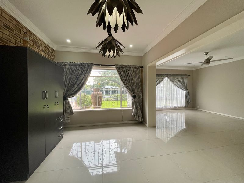 Spacious open-plan living area featuring large windows with security bars, polished tiled floors, decorative pendant lighting, and a neutral color palette.