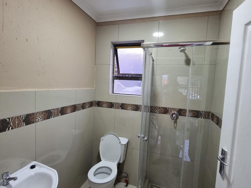 A functional bathroom featuring a pedestal basin, toilet, and a glass-enclosed shower with decorative tiled accents and neutral wall finishes.
