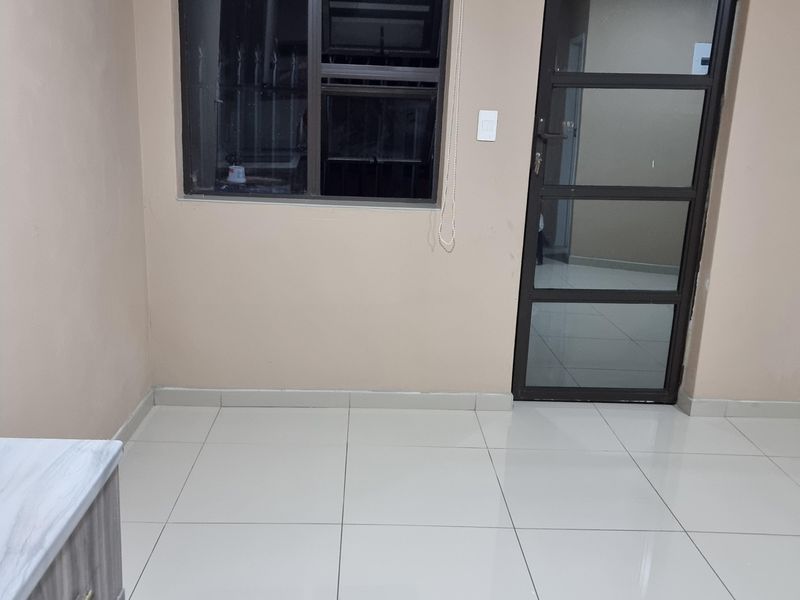 A clean, empty living area featuring neutral wall tones, large format floor tiles, and modern aluminium-framed windows and doors.