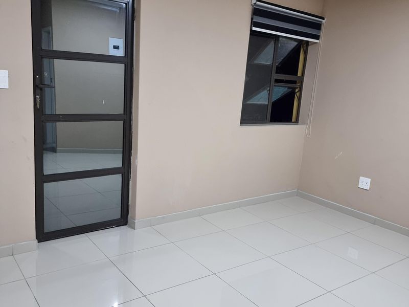 A clean, empty living space featuring neutral wall tones, large format floor tiles, and modern aluminium window and door frames.