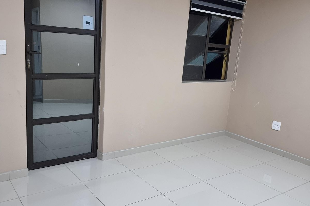 A clean, empty living space featuring neutral wall tones, large format floor tiles, and modern aluminium window and door frames.