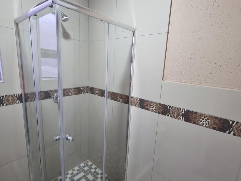 A clean bathroom featuring a glass shower enclosure with tiled walls and a decorative border accent.