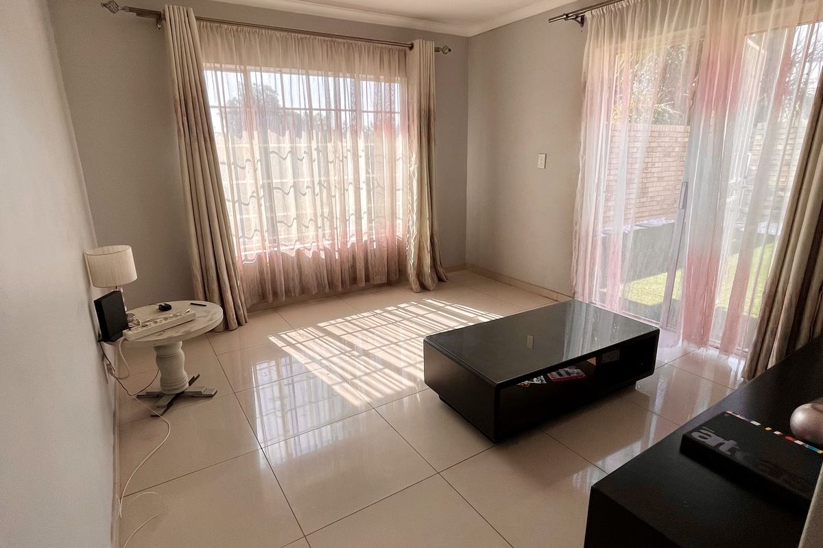 A bright living room featuring large windows, sliding glass doors leading to the exterior, and neutral tiled flooring throughout.