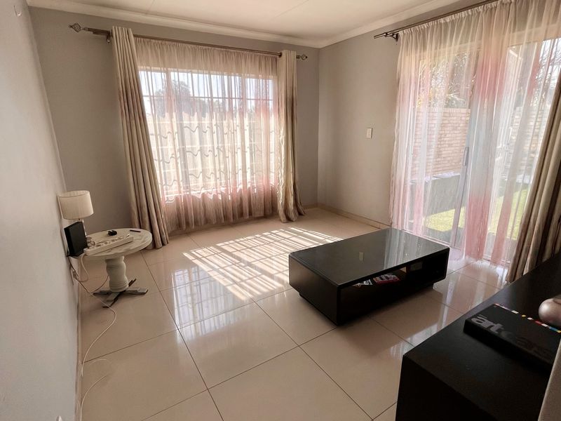 A bright living room featuring large windows, sliding glass doors leading to the exterior, and neutral tiled flooring throughout.