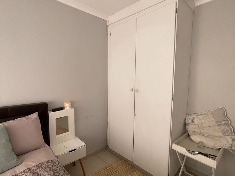 A bedroom featuring neutral wall paint, tiled flooring, and a built-in white wardrobe providing essential storage space.