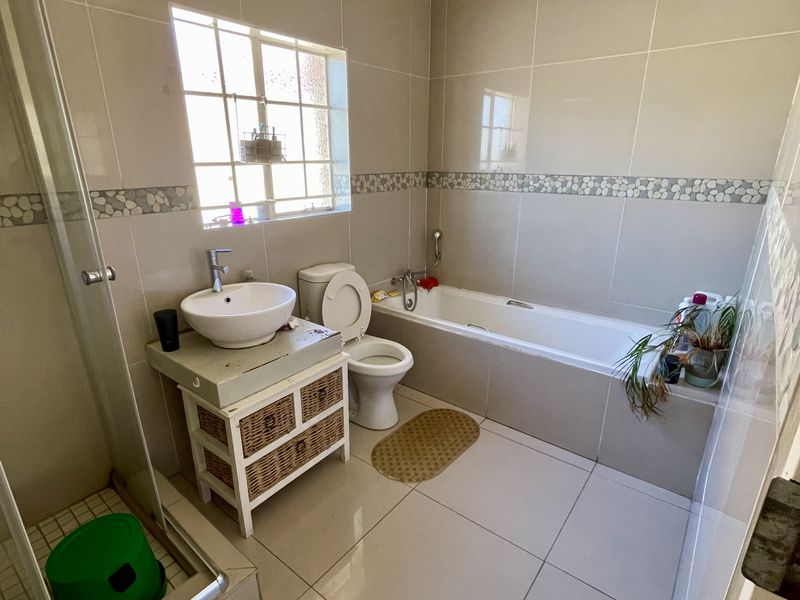 A functional bathroom featuring a shower enclosure, bathtub, toilet, and basin with tiled finishes throughout.