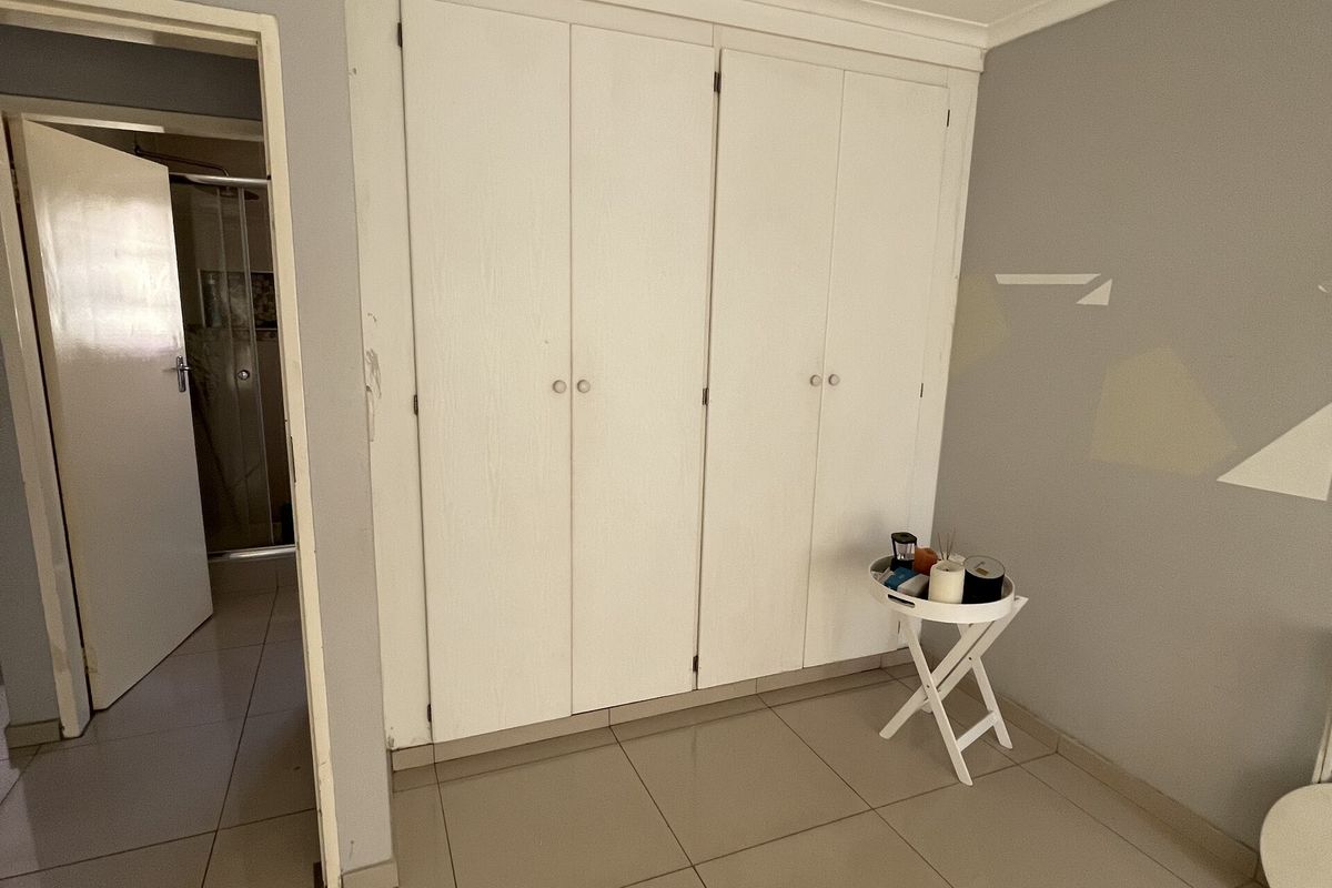 A bedroom featuring built-in cupboards, tiled flooring, and neutral wall finishes, with an adjacent doorway leading to a bathroom area.