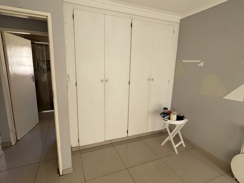 A bedroom featuring built-in cupboards, tiled flooring, and neutral wall finishes, with an adjacent doorway leading to a bathroom area.