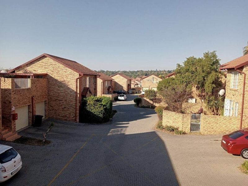 An elevated view of a townhouse complex featuring face brick exteriors, paved driveways, and established landscaping within a residential estate.