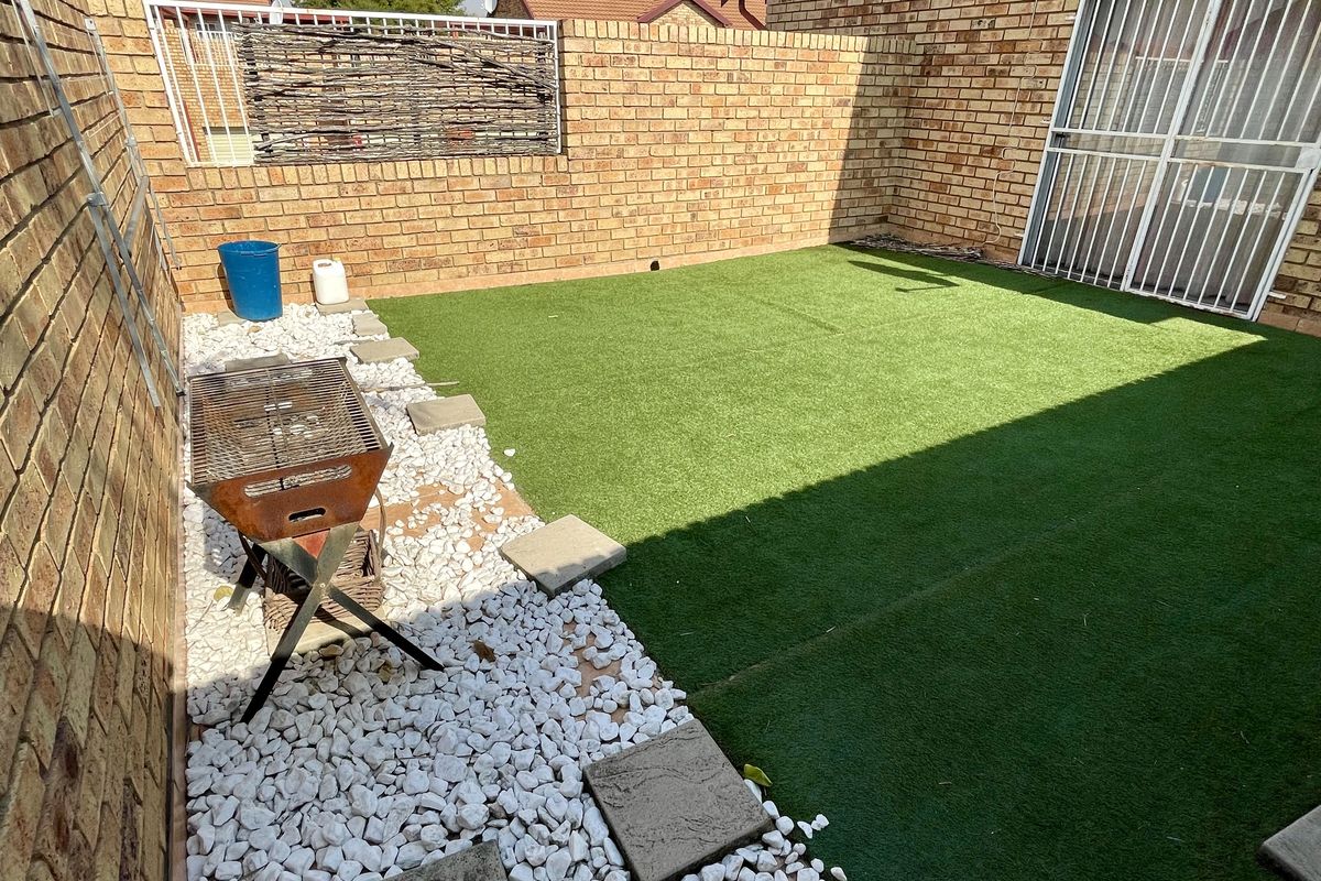 A private rear courtyard featuring artificial turf, stone landscaping, and a secure gated entrance to the townhouse.