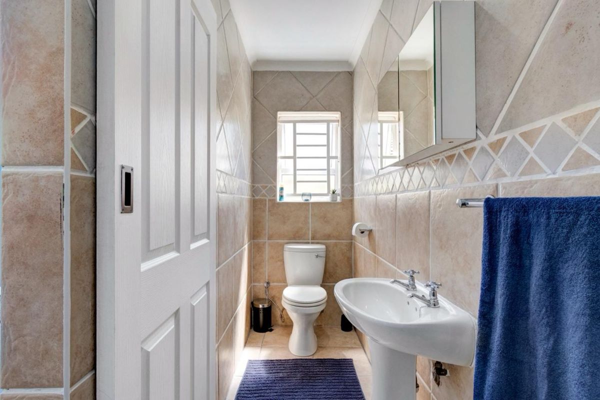 A compact guest bathroom featuring floor-to-ceiling tiled walls, a pedestal basin, a wall-mounted medicine cabinet, and a standard toilet.