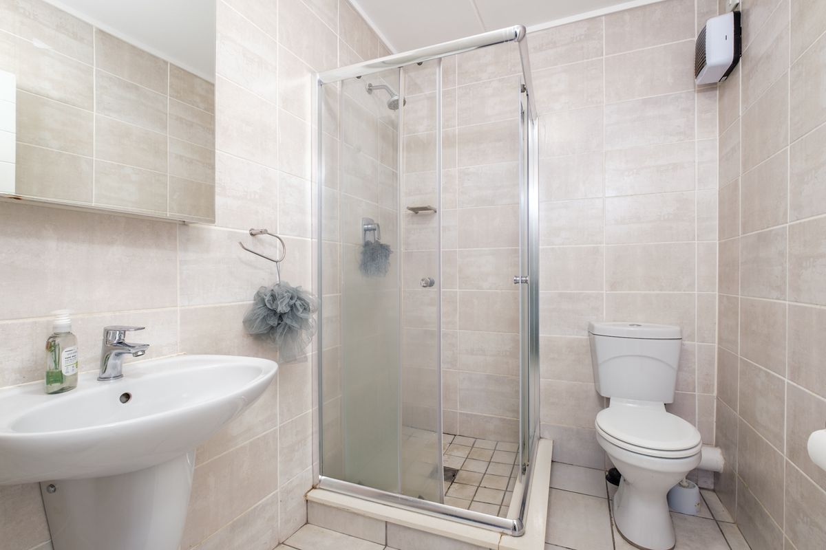 A functional bathroom featuring a pedestal washbasin, a glass-enclosed shower, and a standard toilet, finished with neutral wall and floor tiling.