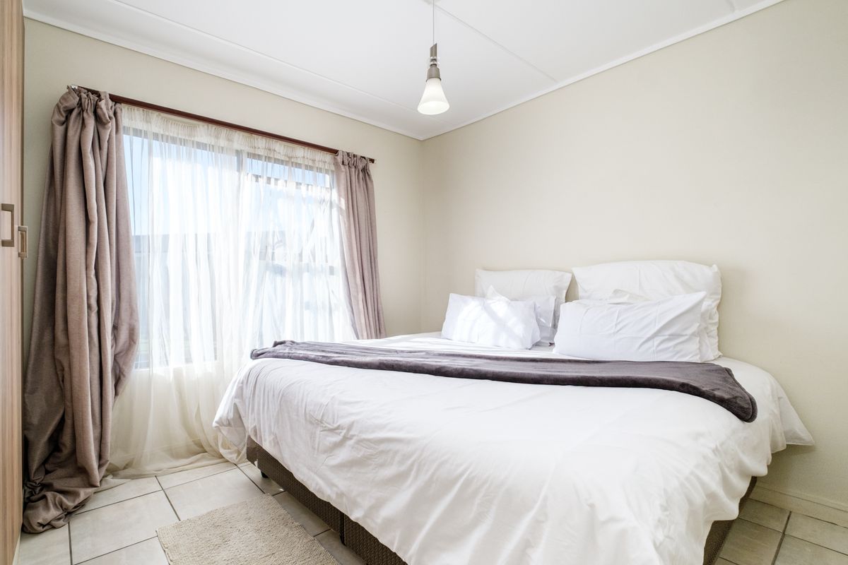A bright and well-maintained bedroom featuring tiled flooring, a built-in wardrobe, and a large sliding window that allows for ample natural light.