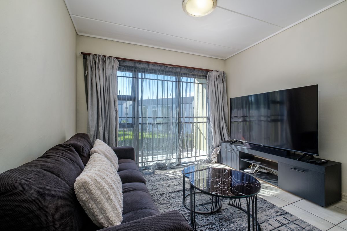 A comfortable living room featuring tiled flooring and a large sliding glass door that provides access to an outdoor balcony area.
