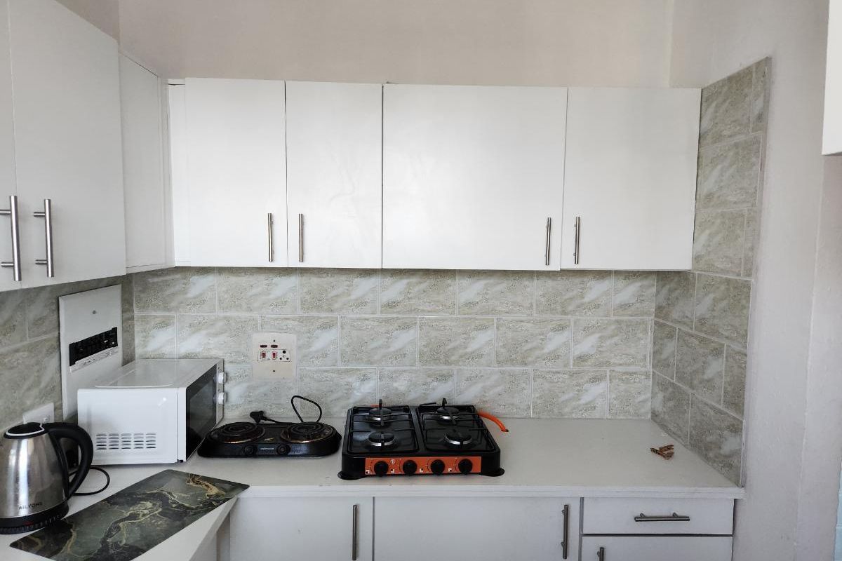 A compact kitchen featuring white built-in cabinetry, a tiled backsplash, and a functional gas hob set into the countertop.