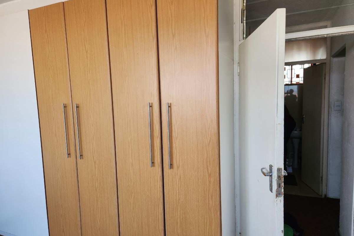 A bedroom featuring built-in wooden cupboards and an open doorway leading to an adjacent room.