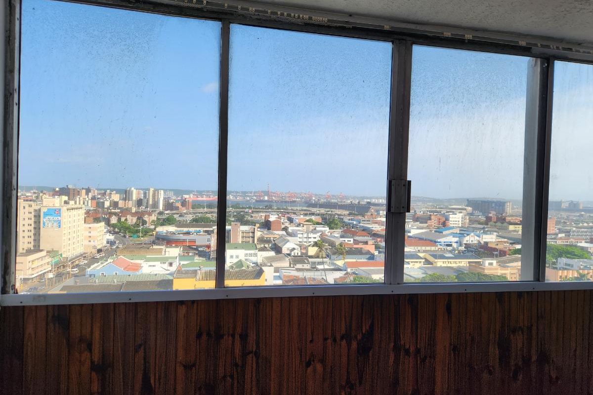 An elevated view of the city skyline and harbor area captured through a large window with wood paneling below.
