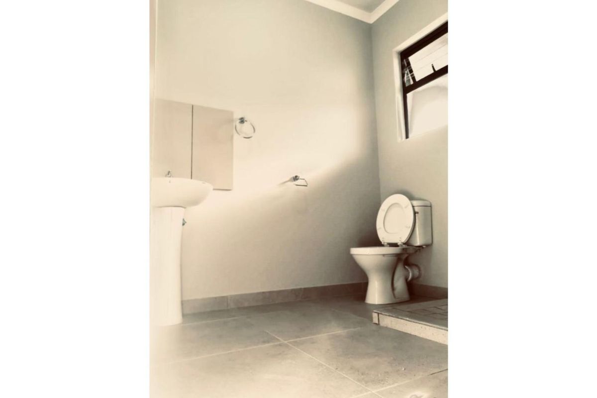 A simple, empty bathroom featuring a pedestal basin, toilet, and tiled flooring with natural light from a side window.