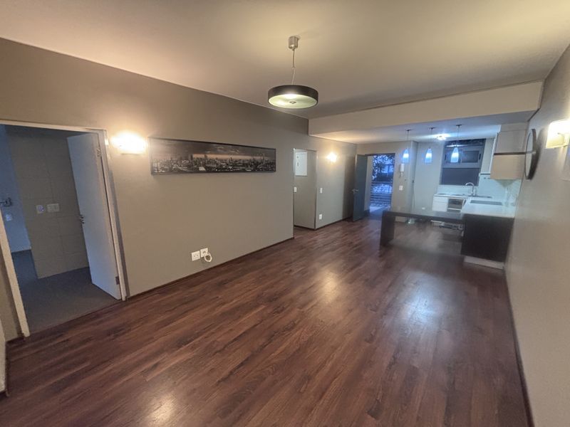 Spacious open-plan living area featuring dark laminate flooring, neutral walls, and an integrated kitchen space with modern cabinetry and lighting.
