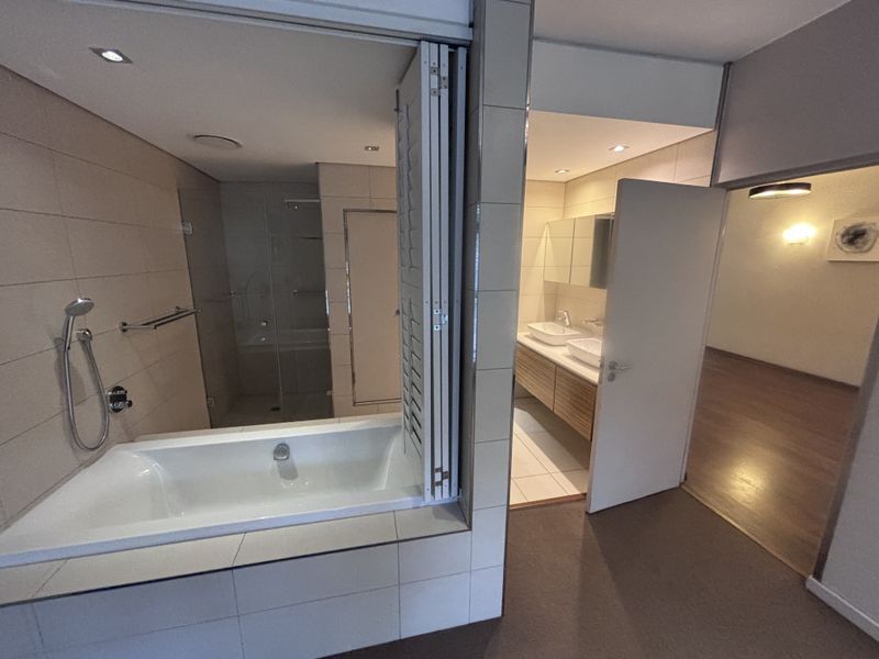 Modern bathroom featuring a built-in bathtub, glass shower enclosure, and a double vanity with integrated storage, finished with neutral wall and floor tiling.