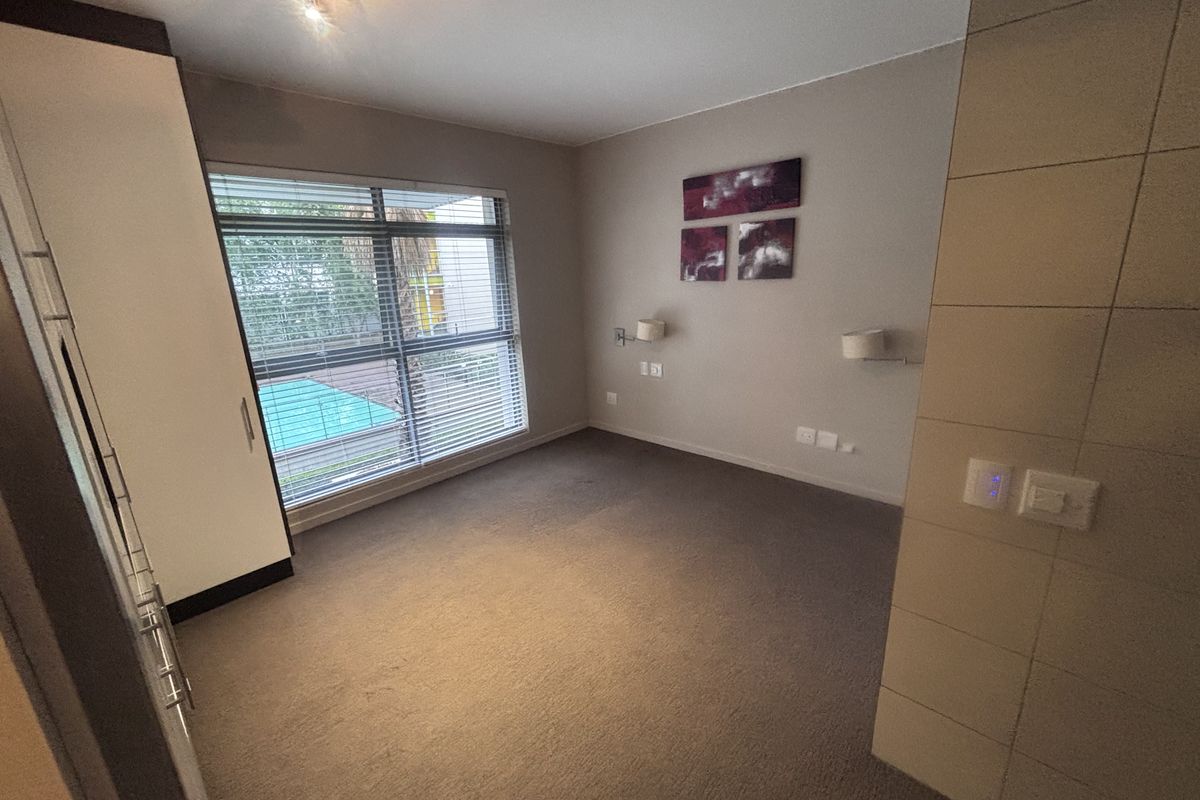A spacious bedroom featuring neutral carpeting, a built-in wardrobe, and a tiled feature wall, offering a clean and functional living space.