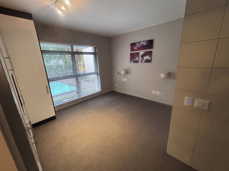 A spacious bedroom featuring neutral carpeting, a built-in wardrobe, and a tiled feature wall, offering a clean and functional living space.