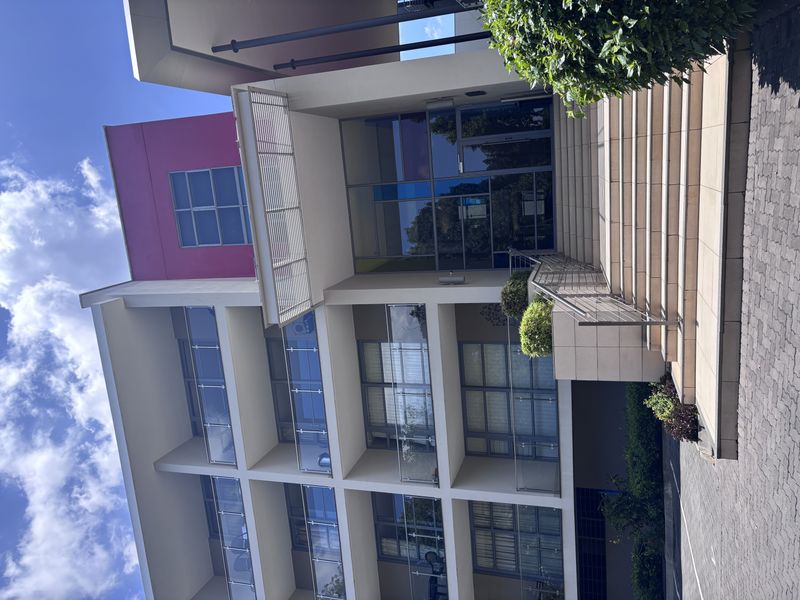 Front facade of a modern multi-story apartment building featuring glass balconies, a tiled entrance staircase, and a paved driveway.