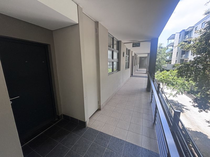 An open-air apartment building corridor featuring tiled flooring, metal safety railings, and access to residential units.