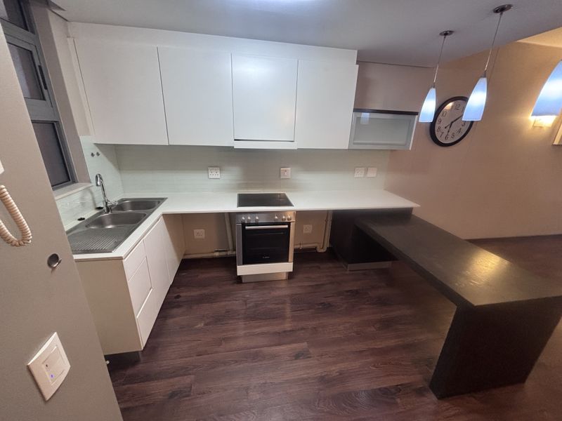 Modern kitchen featuring white cabinetry, integrated electric oven and hob, stainless steel sink, and a dark wood-look breakfast bar with pendant lighting.