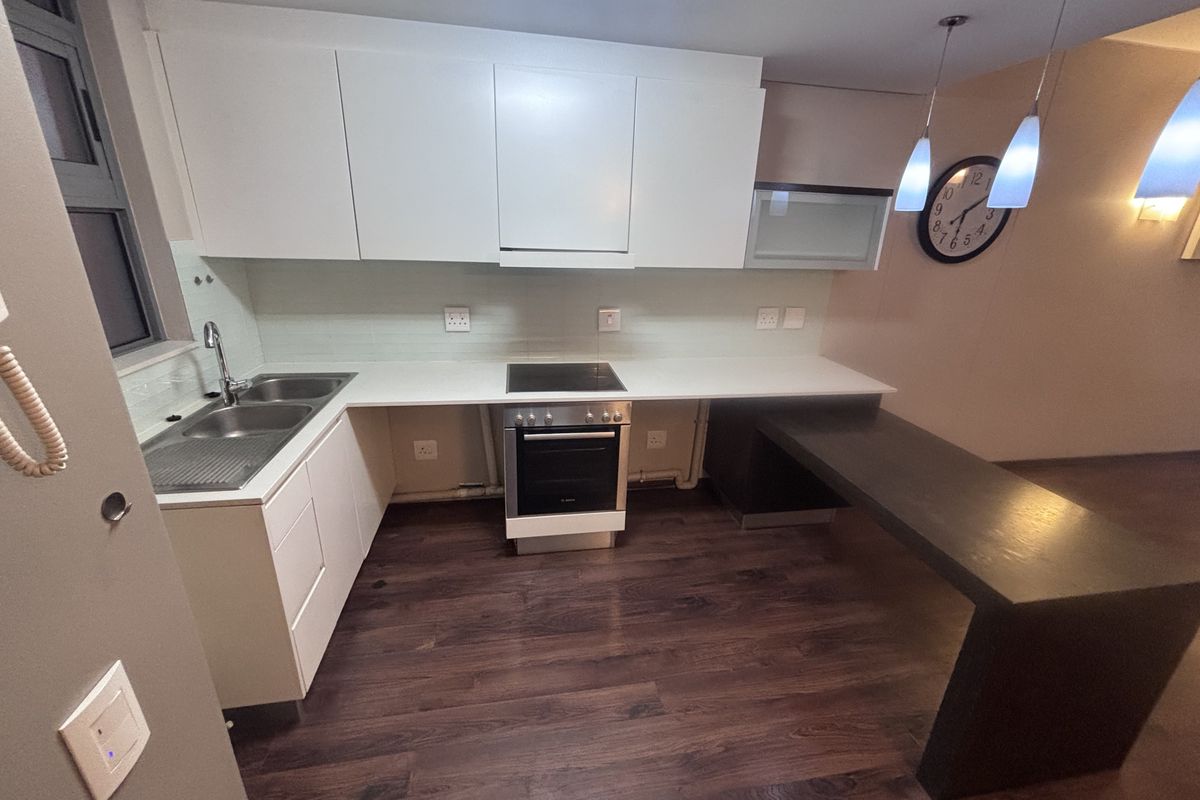 Modern kitchen featuring white cabinetry, integrated electric oven and hob, stainless steel sink, and a dark wood-look breakfast bar with pendant lighting.