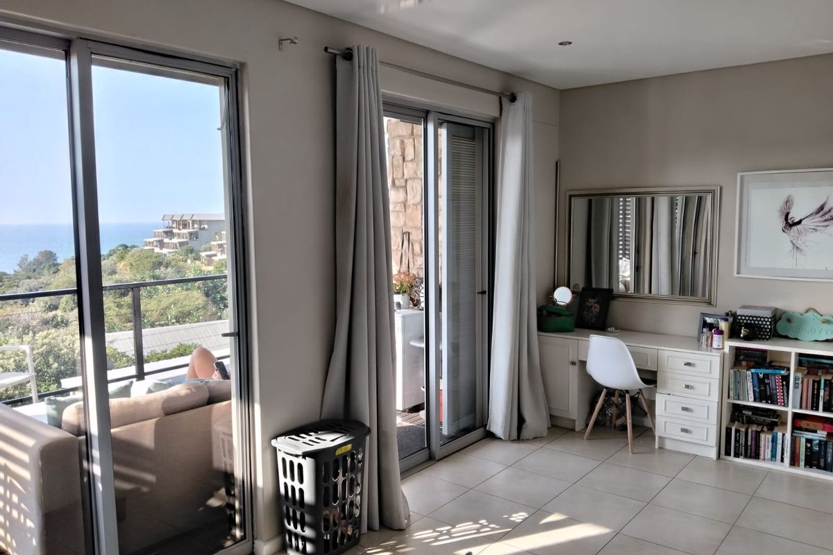 A bright bedroom featuring tiled floors, a built-in vanity, and large sliding glass doors that open onto a balcony with ocean views.