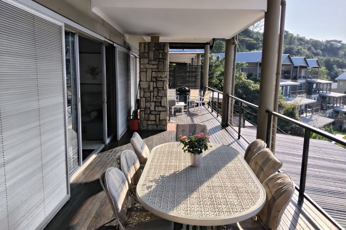 Spacious covered balcony featuring timber decking, stone-clad structural pillars, and sliding glass door access to the interior living area.
