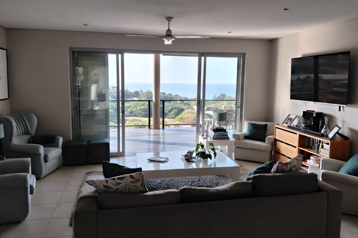 Spacious living room featuring large sliding glass doors that open onto a balcony with scenic coastal views and abundant natural light.