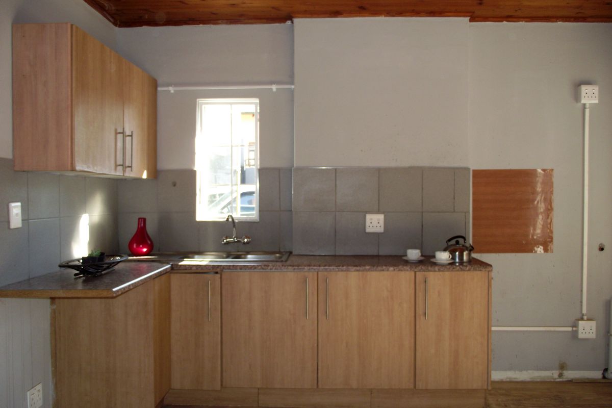 A functional kitchen featuring laminate cabinetry, a stainless steel sink, and a timber ceiling, currently awaiting cosmetic updates to improve its overall aesthetic appeal.
