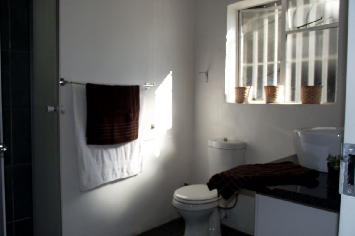 A functional bathroom featuring a vanity with basin, toilet, and shower enclosure, finished with dark floor tiles and security bars on the window.