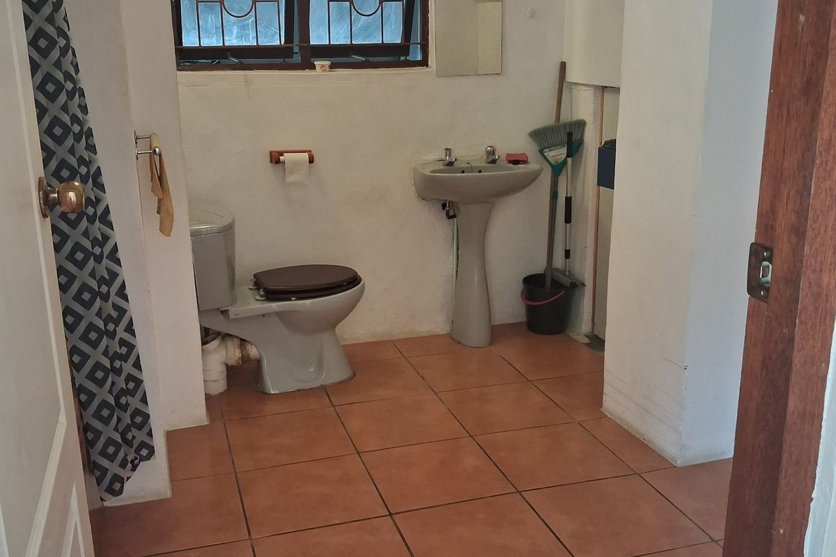 A compact bathroom featuring a pedestal basin, toilet, and tiled flooring, situated under a sloped ceiling with security bars on the window.