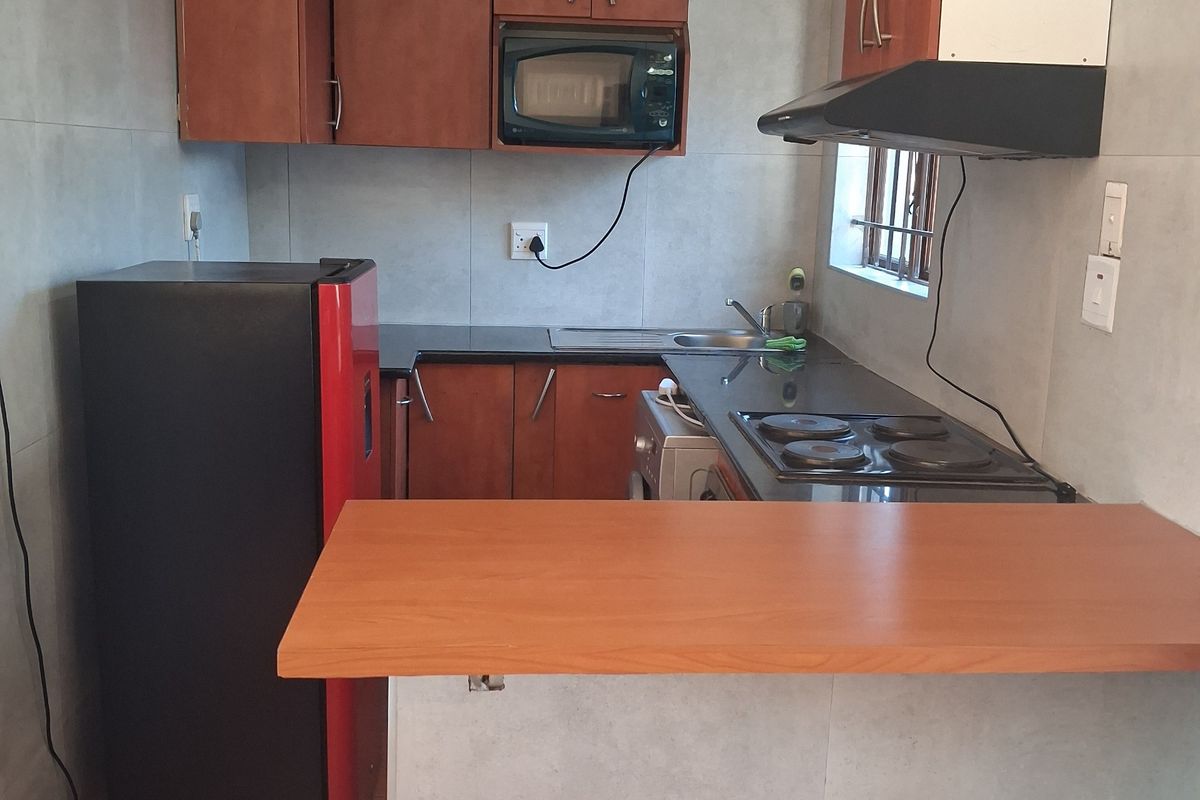 Compact kitchen featuring built-in cabinetry, laminate countertops, an electric hob with extractor fan, and tiled wall finishes.