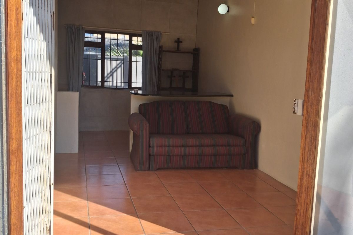 A living area featuring tiled flooring, a ceiling fan, and a built-in counter, accessible through a timber door frame with a security gate.