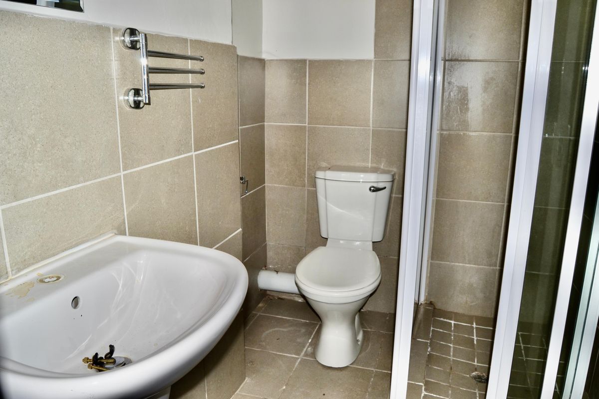 A compact bathroom featuring a pedestal basin, a standard toilet, and a shower enclosure with tiled walls and flooring.