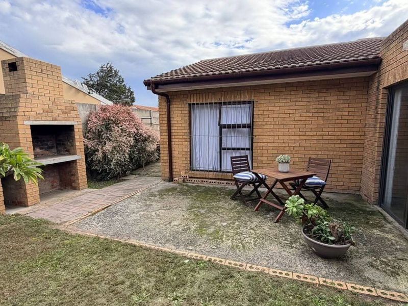 A rear garden area featuring a built-in brick braai, paved patio space, and direct access to the home via sliding glass doors.