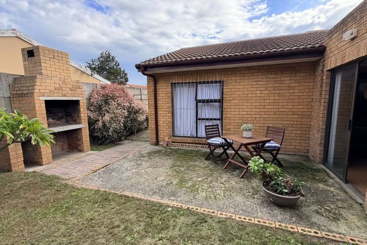 A rear garden area featuring a built-in brick braai, paved patio space, and direct access to the home via sliding glass doors.