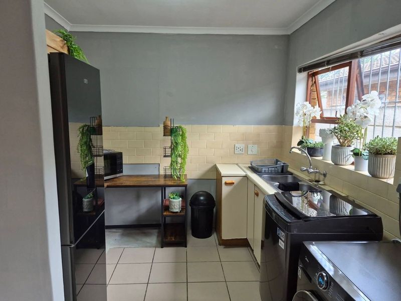 A functional kitchen featuring tiled splashbacks, double sink, and built-in cabinetry with space for laundry appliances.