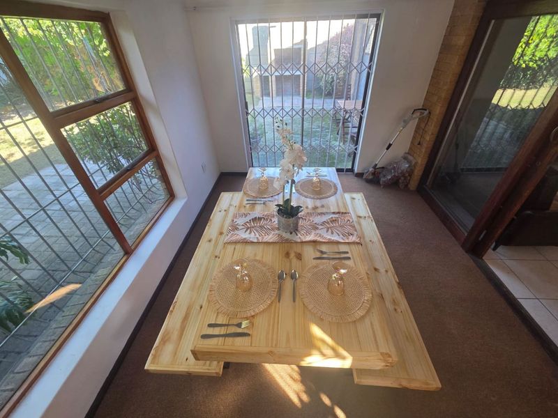 A bright dining area featuring large windows, carpeted flooring, and direct access to the rear garden through a security-gated sliding door.