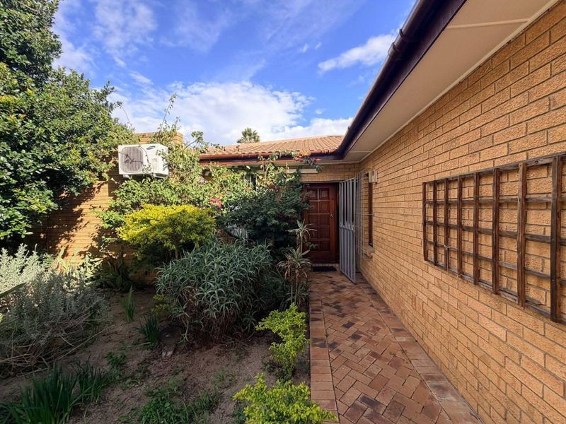 A side exterior view of the house featuring a brick pathway, timber trellis, and an outdoor air conditioning unit.